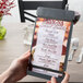 A hand using a Menu Solutions ash wood menu board with rubber band straps on a table.