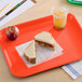 A bright orange plastic fast food tray holding a sandwich, an apple, and a cup of iced drink.