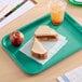 A teal plastic fast food tray holding a peanut butter and jelly sandwich, an apple, and a cup of iced beverage.
