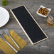 A weathered walnut wood menu board with picture corners on a table with a white plate and bowl of nuts.