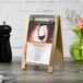A natural wood Menu Solutions sandwich menu board with a clip on a table.