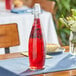 An Acopa clear glass bottle with red liquid on a table.