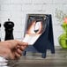 A hand holding a Menu Solutions denim wood menu board tent on a table.