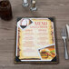 A Menu Solutions weathered walnut wood menu board on a table with a glass of brown liquid and ice.