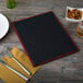 A mahogany wood menu board with silver picture corners on a table with a white plate, fork, and knife.