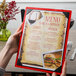 A person holding a Menu Solutions wood menu board with picture corners on a table in a farm-to-table restaurant.