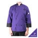 A person wearing a Mercer Culinary purple chef coat on a counter in a professional kitchen.