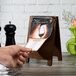 A hand holding a Menu Solutions walnut wood menu board tent clip.