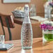 An Acopa textured glass water bottle with a clear swing top lid on a table.