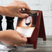 A person uses a mahogany wood Menu Solutions sandwich menu board to cut a menu.