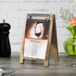 A Menu Solutions weathered walnut wood sandwich menu board tent with a clip on a table with a menu.