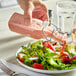 A hand pouring pink liquid from a glass bottle into a salad.