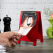 A hand using a Menu Solutions berry wood menu board tent to display a menu on a table.