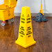 A Rubbermaid yellow cone-shaped caution sign with black text on it.
