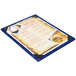 A Menu Solutions True Blue wood menu board with picture corners holding a menu on a table.