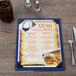 A Menu Solutions wood menu board on a table with a burger and fries and a glass of brown liquid.
