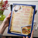 A hand holding a customizable wood menu board with picture corners on a table in a fine dining restaurant.