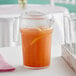 A Cambro stackable pitcher of orange juice with a lemon wedge on a table.