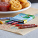 A print box filled with Choice assorted color crayons on a table with a plate of food and crayons.