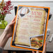 A hand holding a customizable wood menu board with picture corners.