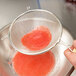 A person using a Tablecraft medium double mesh strainer over a red liquid.