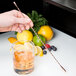 A hand using a Barfly copper plated double end stirrer to mix a drink with lemon slices.