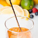 A Barfly copper plated double end cocktail stirrer in a glass with a drink and a straw with a slice of orange.