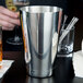 A close-up of a silver Barfly cocktail shaker tin on a table.