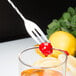 A Barfly stainless steel bar spoon with a fork end stirring a cherry in a glass of liquid.