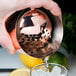 A hand holding a Barfly copper julep strainer pouring a cocktail.