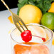 A Barfly gold plated bar spoon with fork end stirring a cocktail with a cherry.