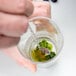 A hand holding a Barfly stainless steel bar spoon in a glass of green liquid.