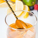 A Barfly gold plated Japanese style bar spoon in a glass of whiskey with a lemon slice.