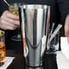 A hand using a Barfly stainless steel cocktail shaker to mix a drink.