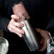 A man holding a Barfly stainless steel cocktail shaker full of a drink.