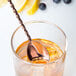 A copper Barfly spoon in a glass of liquid.