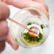 A hand using a Barfly copper plated bar spoon with muddler in a glass of green liquid.