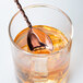 A Barfly copper plated bar spoon with a fork end in a glass of liquid.