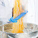 A person using a San Jamar blue plastic bag cutter to squeeze orange liquid into a plastic bag.