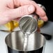 A person using a Barfly stainless steel Japanese jigger to pour liquid into a metal cup.