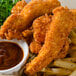 A plate of fried chicken strips and french fries with a bowl of brown sauce on a table.