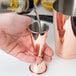 A person using a Barfly copper Japanese style jigger to pour liquid into a cup.