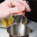 A hand using a copper Barfly Japanese Style Jigger to pour liquid into a metal cup.