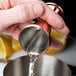 A person using a Barfly copper jigger to pour liquid into a metal cup.