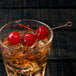 A glass of whiskey with a Barfly copper cocktail pick with a circle top holding cherries.