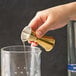A hand using a Barfly gold-plated Japanese style jigger to pour liquid into a glass.