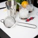 A metal strainer and a metal cup on a white surface.