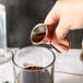 A hand using a Barfly copper jigger to pour liquid into a glass.