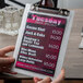 A person holding a Menu Solutions Alumitique menu board with a red surface in the background.