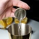 A person using a Barfly gold-plated Japanese style jigger to pour liquid into a metal cup.